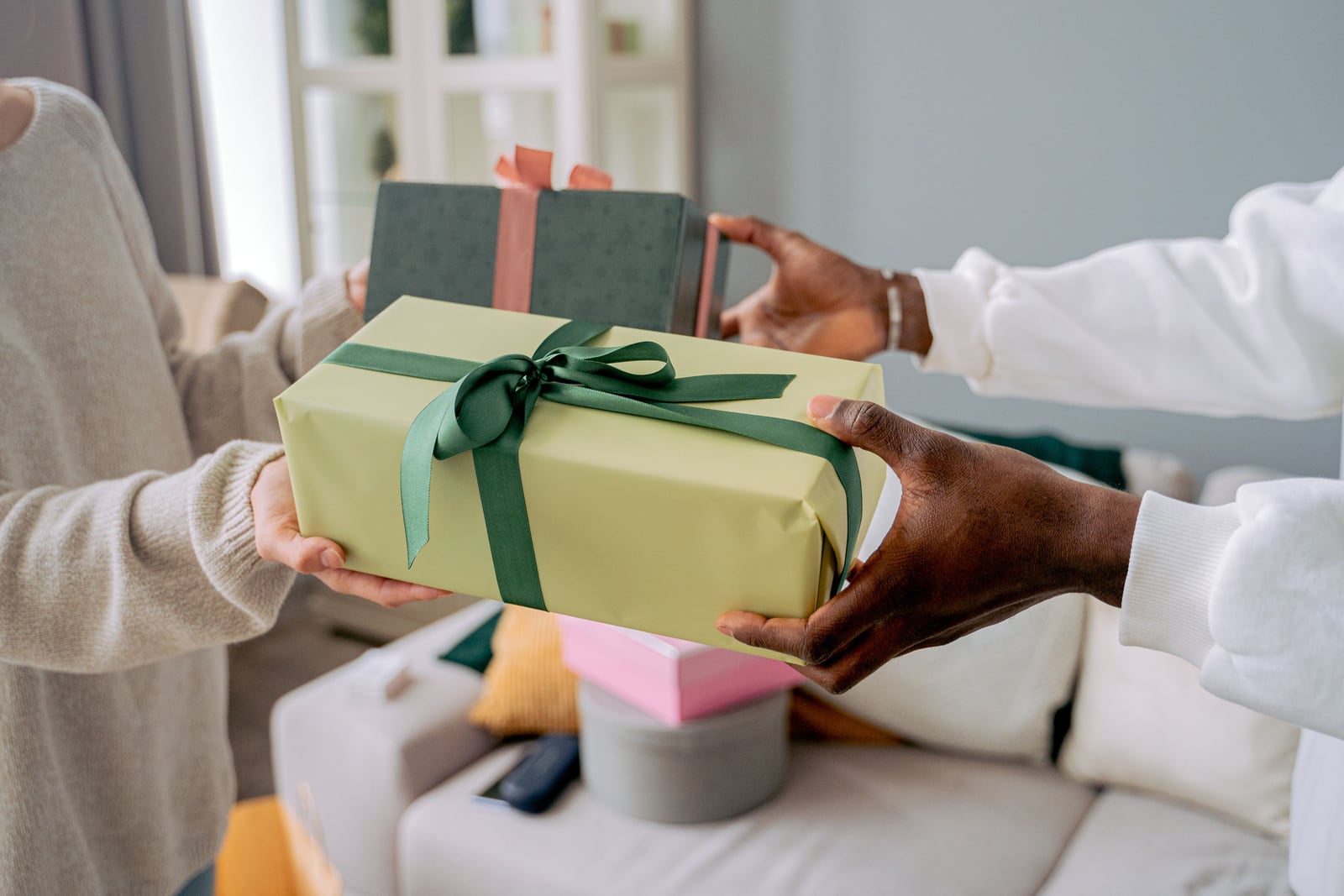 Two people exchange wrapped gifts in a softly lit living room, with a second ribboned present nearby.