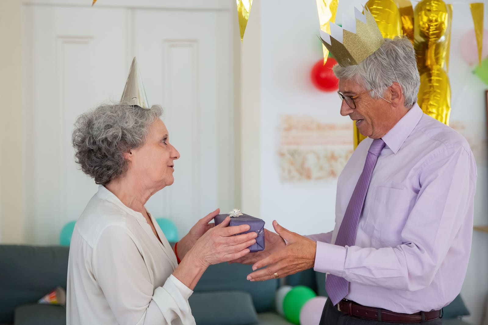 An older man reaches for a small wrapped gift being offered during an indoor celebration.
